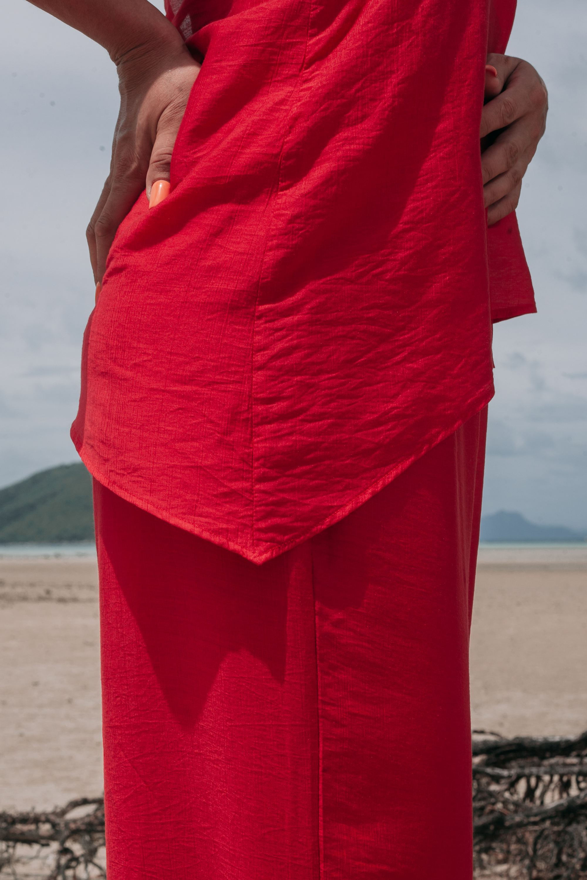 Close-up side view of Carmine Top by INNEVIA in deep red, highlighting the elongated flowing side detail and lightweight fluid fabric