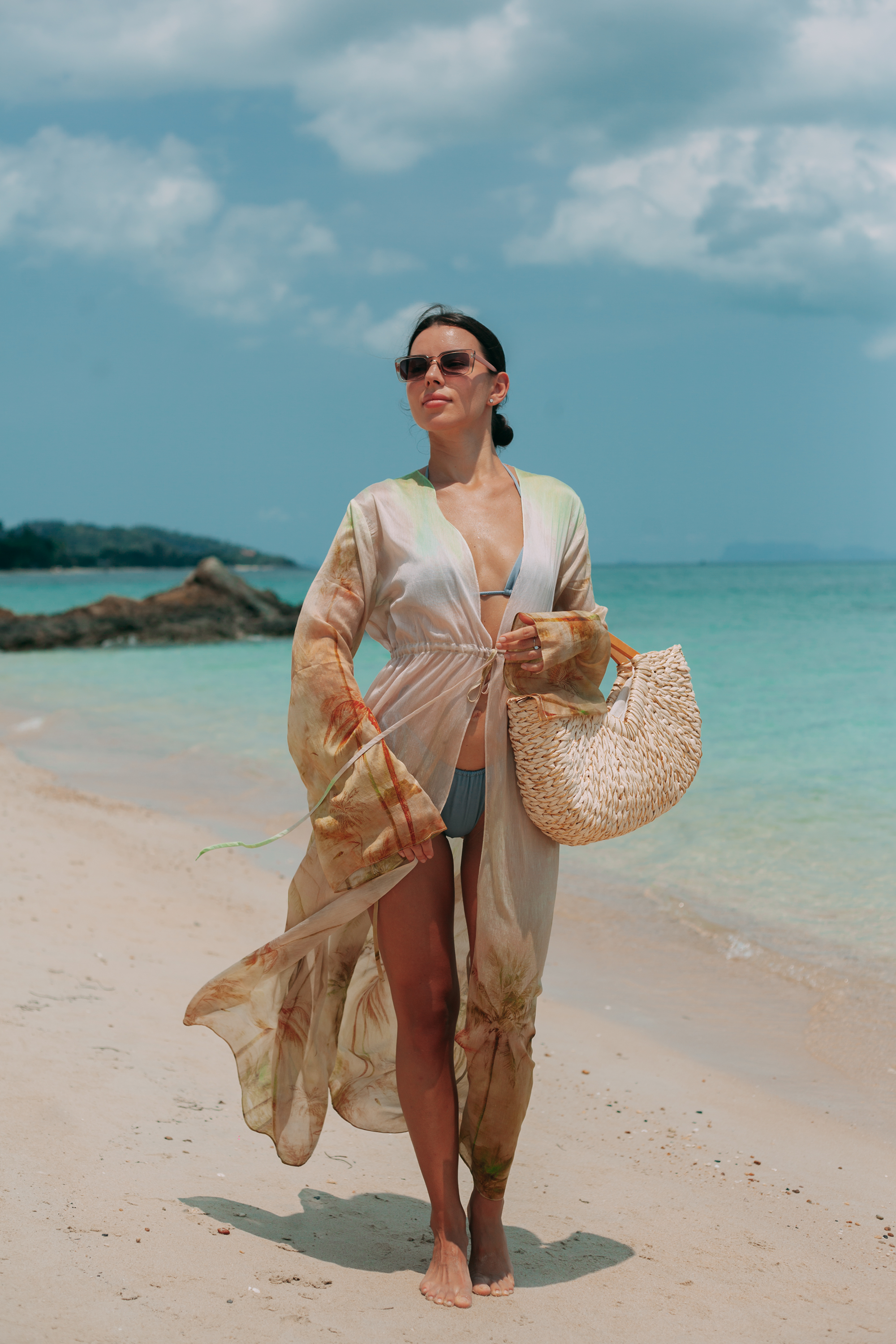 Woman wearing Selara Maxi Tunic in a tropical print walking along a white sand beach