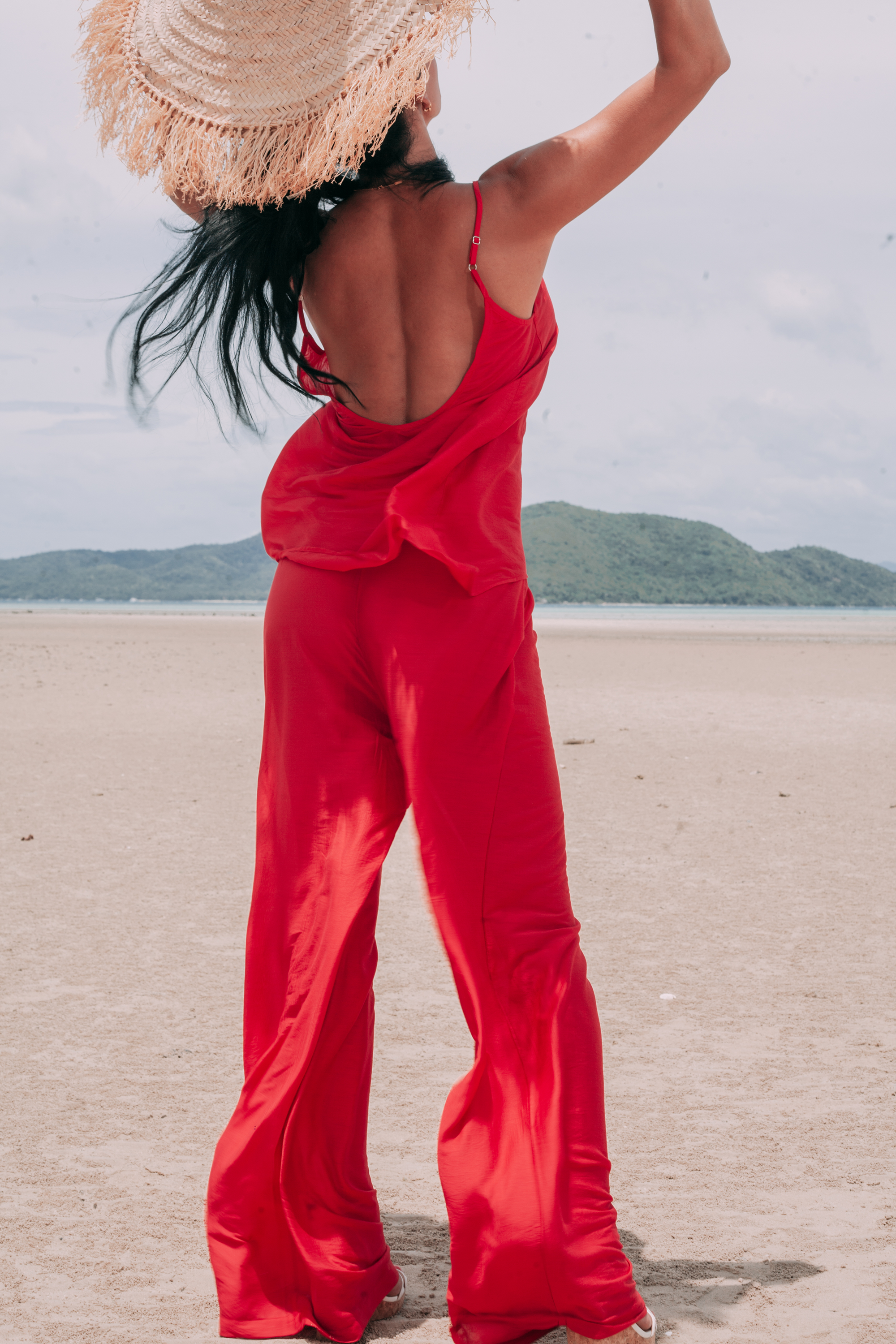 Back view of Carmine Fluid Pants by INNEVIA, deep red flowing wide-leg trousers styled with the matching Carmine Top by the sea