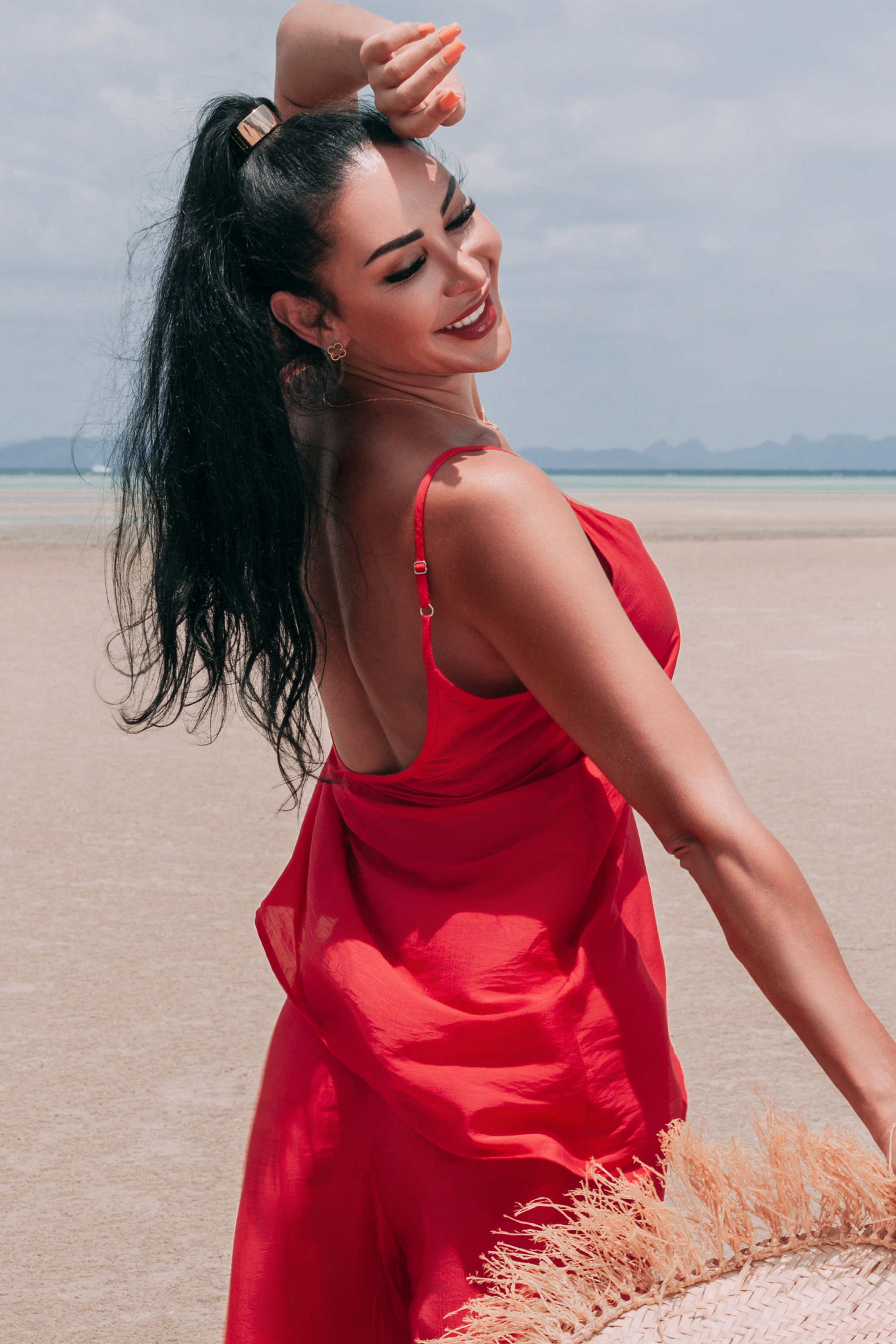 Side view of Carmine Top by INNEVIA in deep red, showing the relaxed fluid silhouette and adjustable slim shoulder straps at the beach