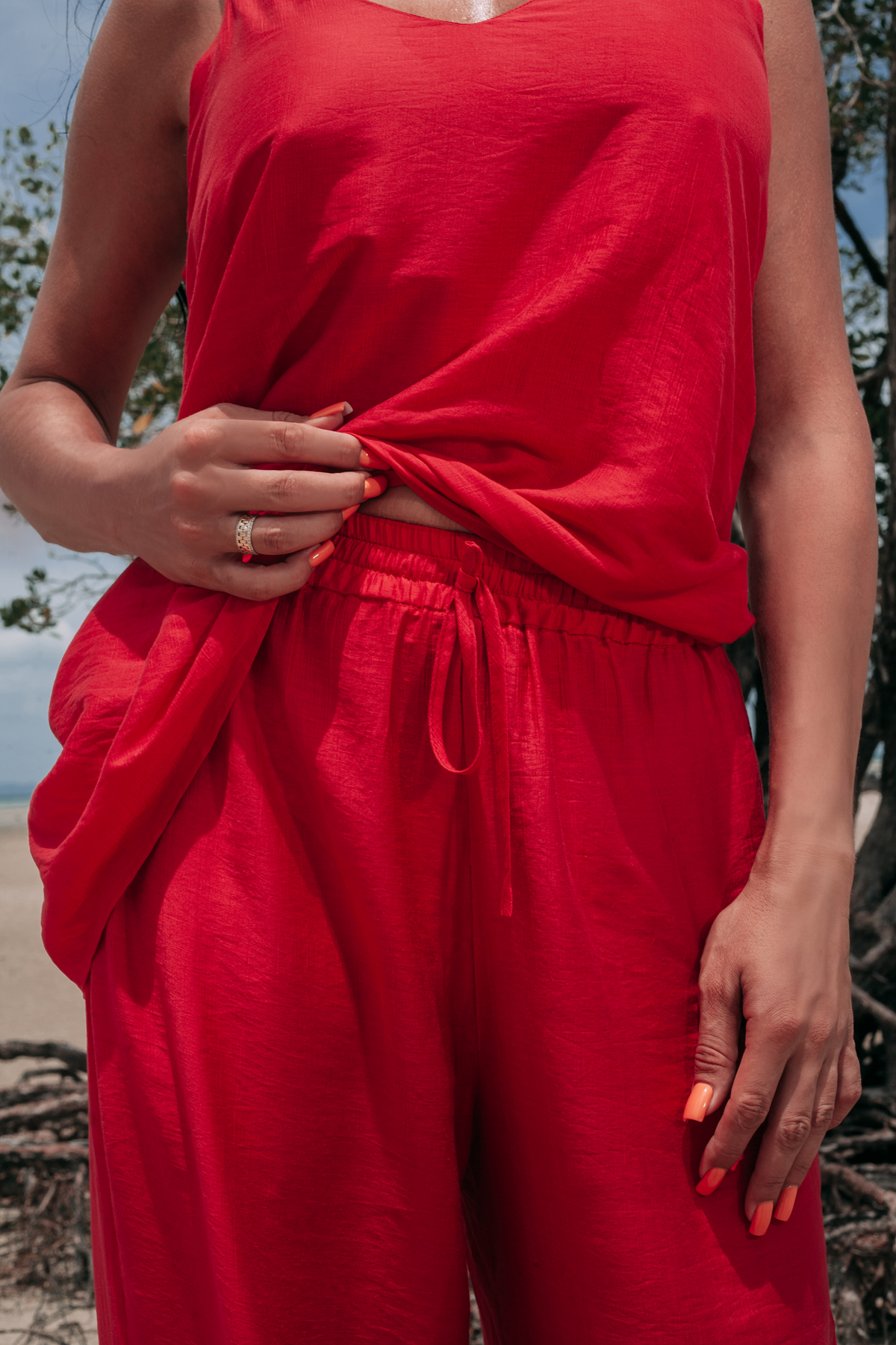 Close-up of Carmine Fluid Pants by INNEVIA showing the lightweight deep red fabric, soft drape and relaxed trouser silhouette